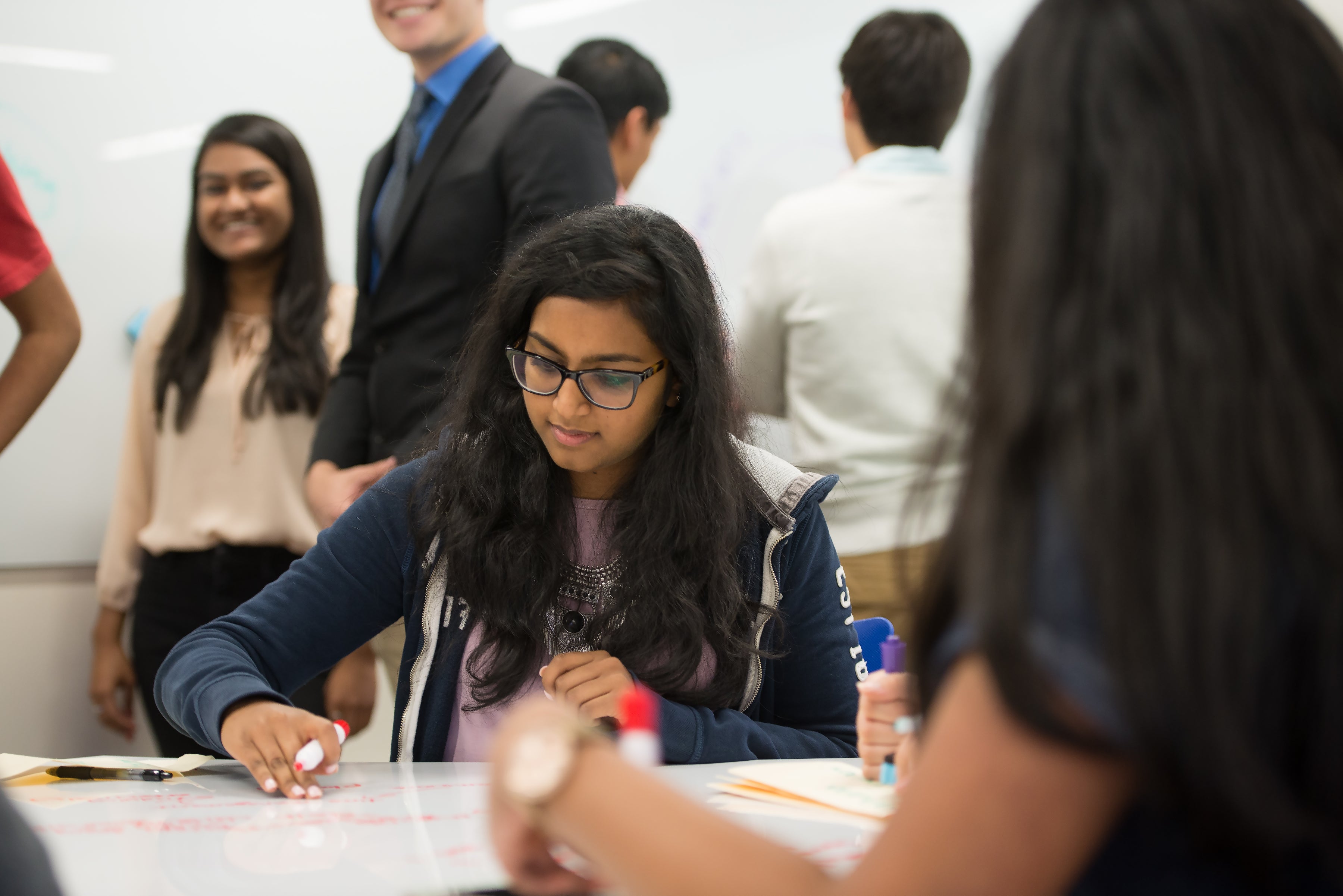A student sitting at a table and writing on a handheld whiteboard