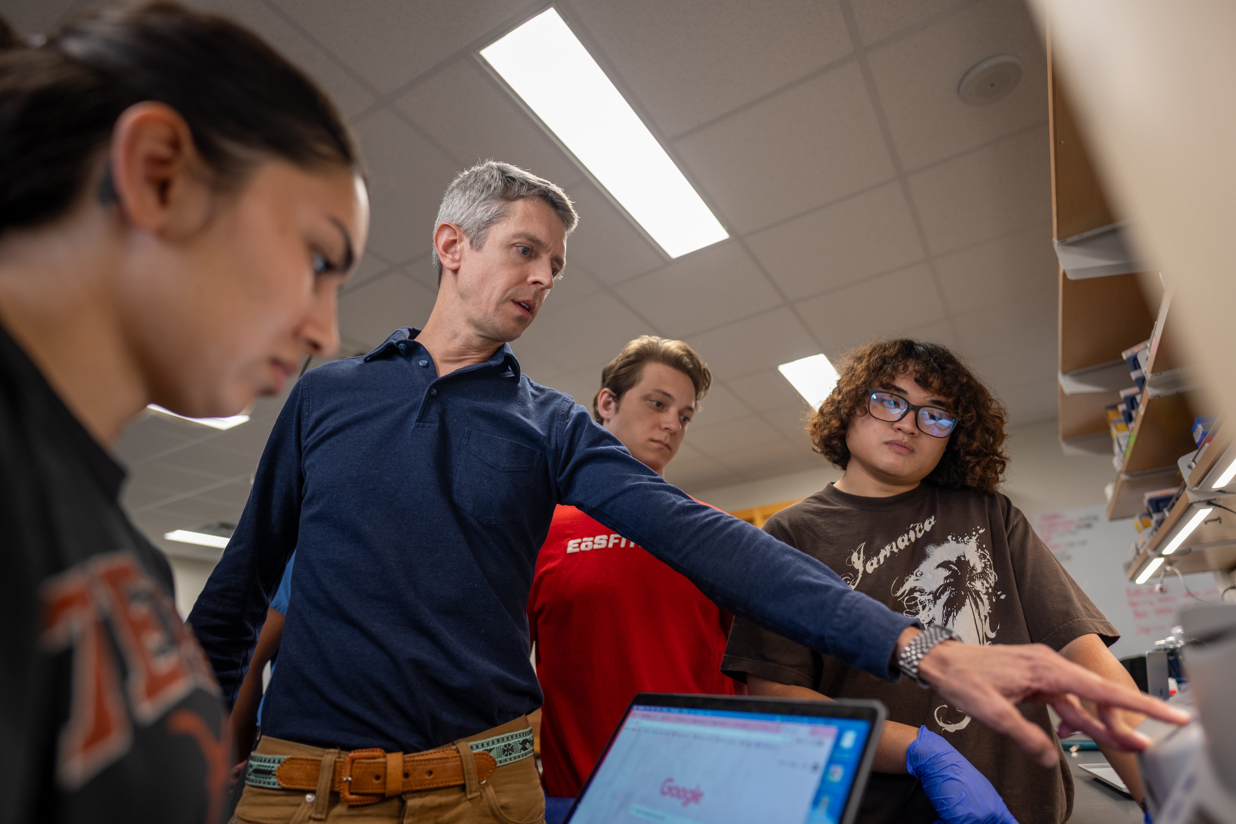 A faculty instructor teaching three students how to use lab technology. 